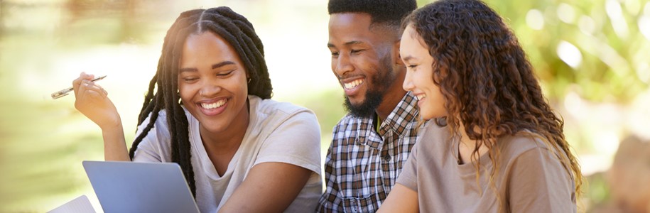 Group of diverse college friends studying outdoors on a shared laptop under the bright sun.